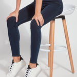 color=Indigo, Front angle, seated view of indigo  toothpick denim jean leggings with patented concealed waistband